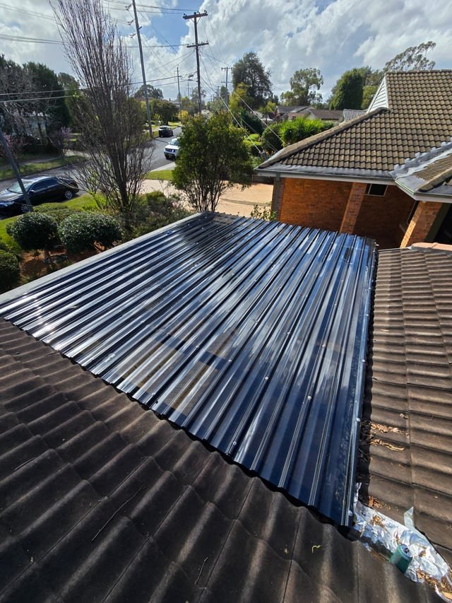 Sydney roofer kneeling on a tile roof inspecting ridgecaps with tools beside him